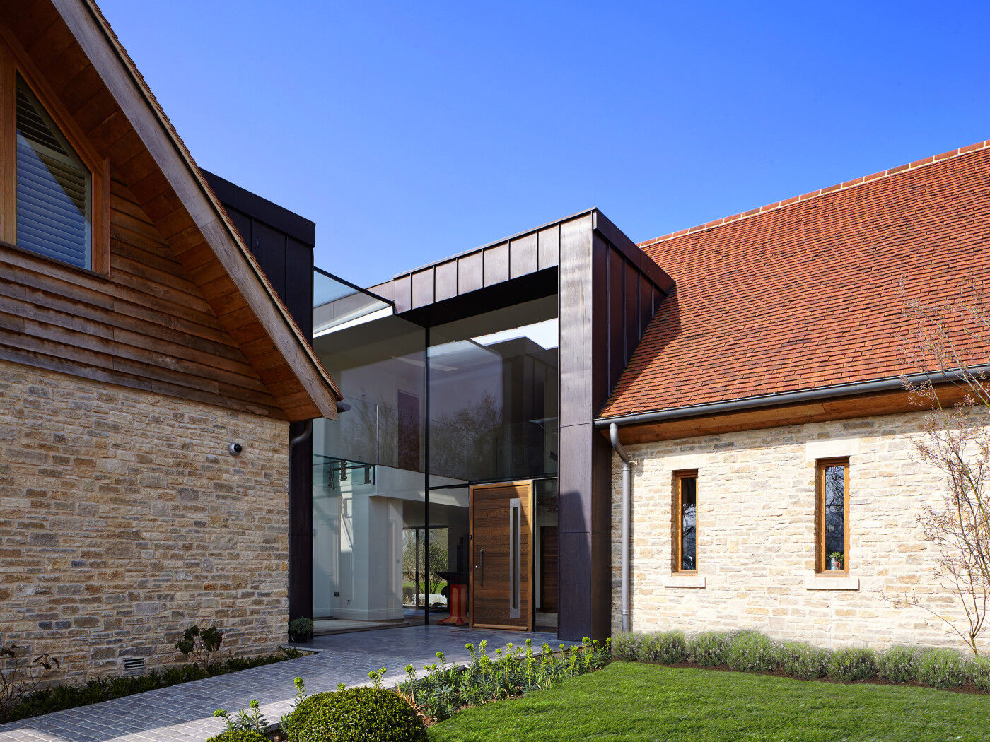 The glass of this facade dominates the entrance way but the fumed oak front door is the standout element bringing the variety of mixed building materials together 
