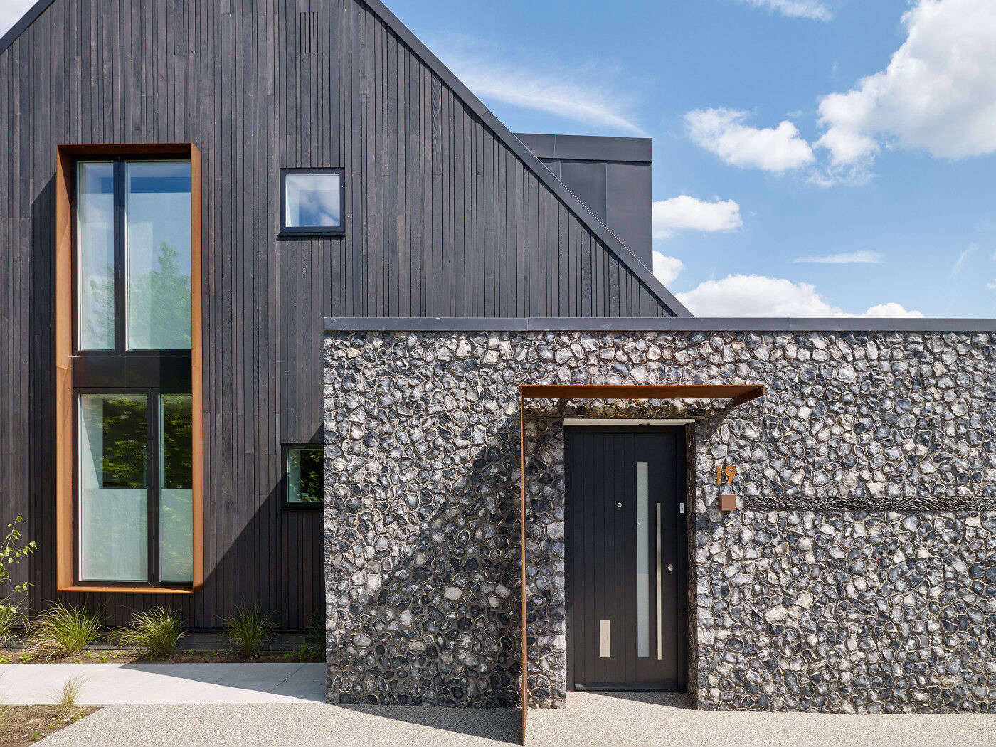 In this case, although the black door matches the cladding, the look is broken up with stone, a weathered steel canopy & a sleek steel handle