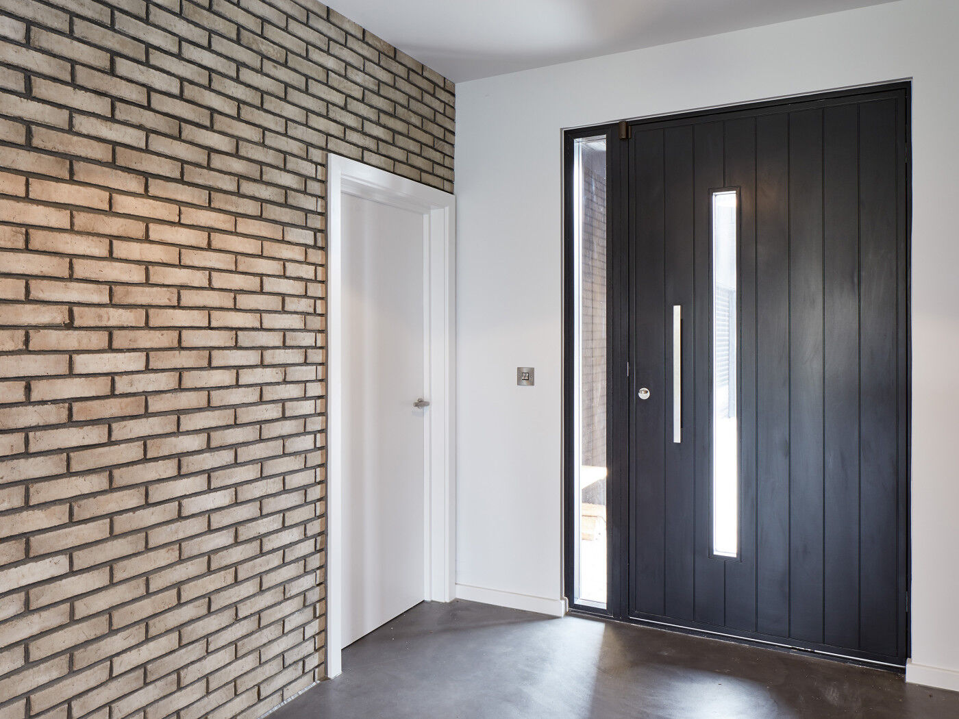 The brick wall & bright white paint nicely highlights the contemporary black door in this hallway