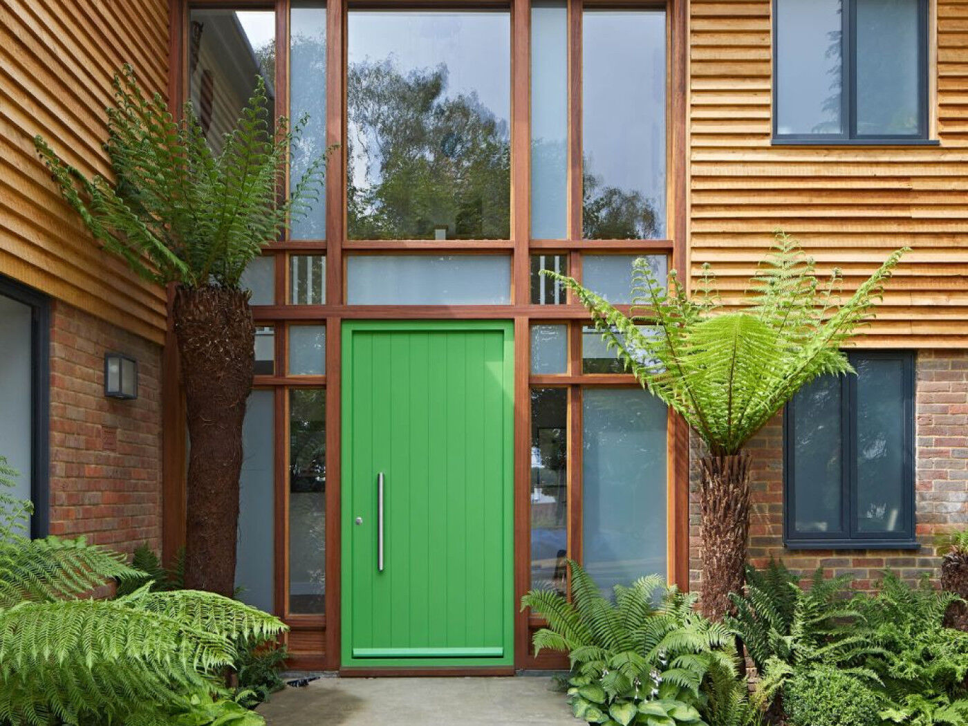 This green door looks amazing with wood cladding and tropical planting