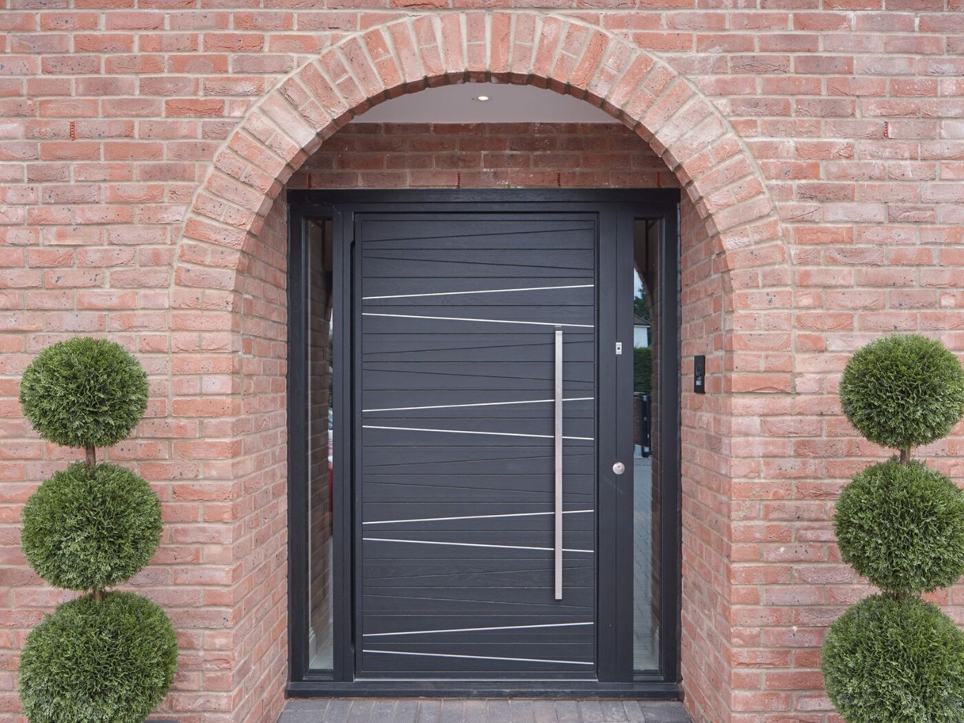 Pale red brick, symmetrical trees and a curve help the dark grey door with silver detailing stand out.