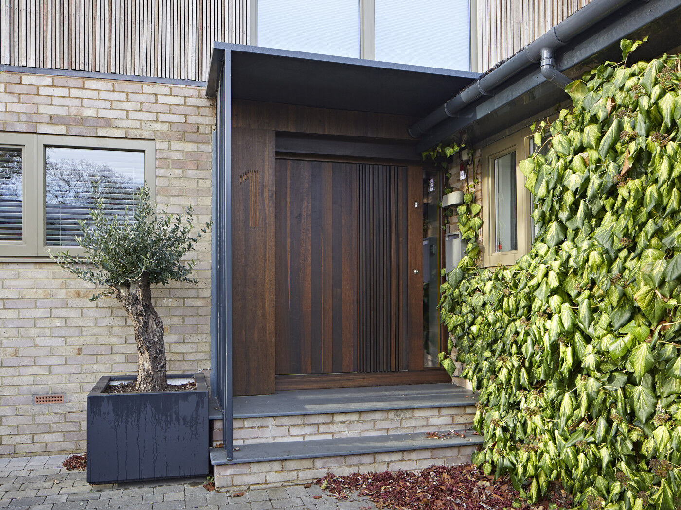 The fumed oak door stands out against the pale bricks and olive window frames.