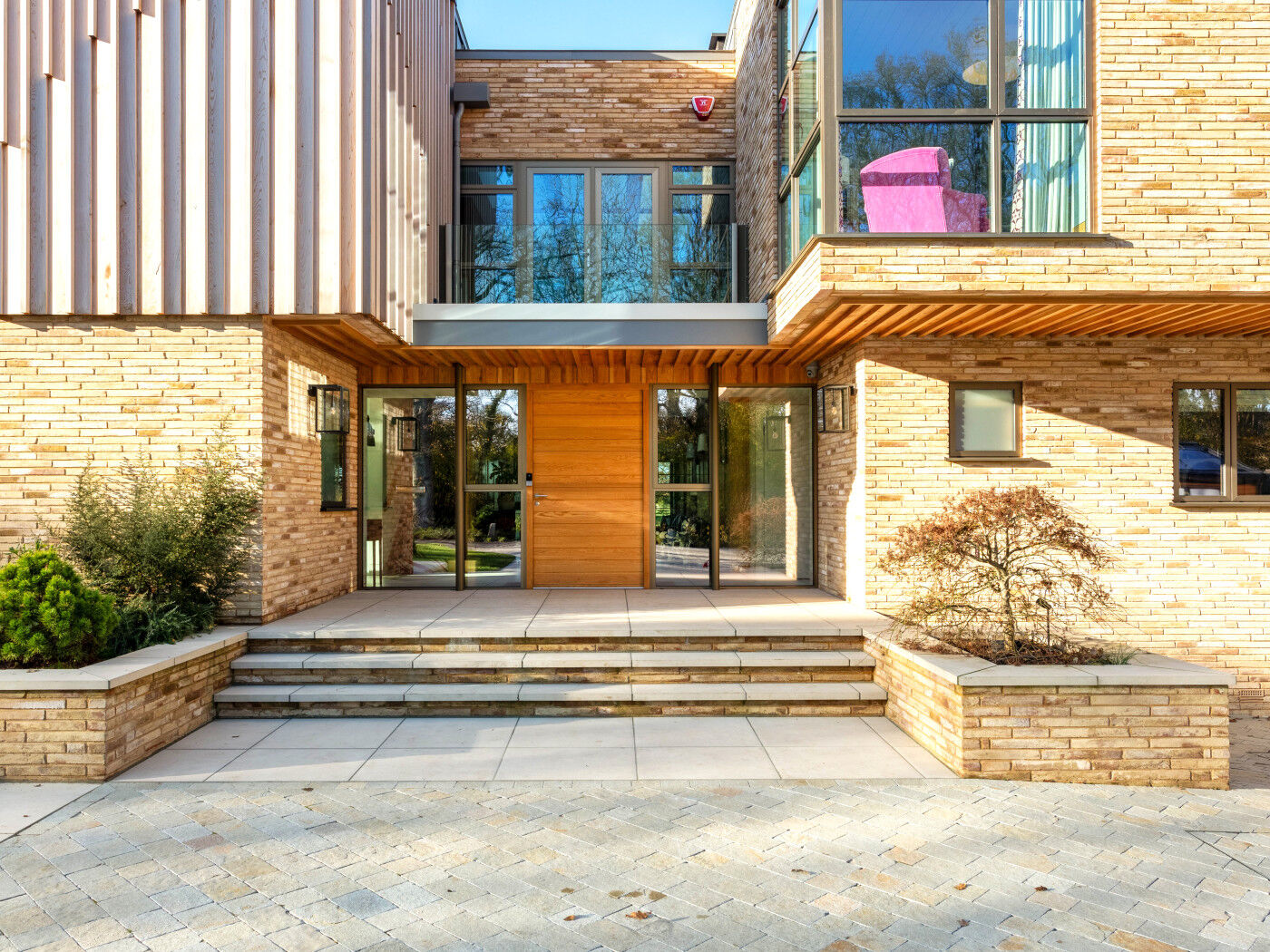 Soft green window frames, yellow bricks and a warm oak door in a contemporary new build home.