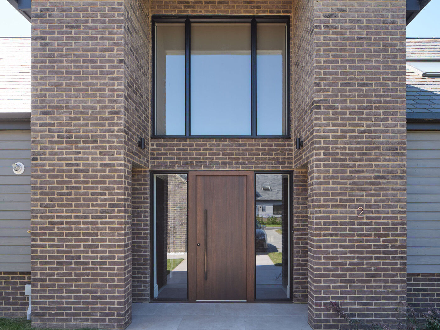 Full of drama, this double height entrance blends dark window frame, fumed oak, and brown bricks.