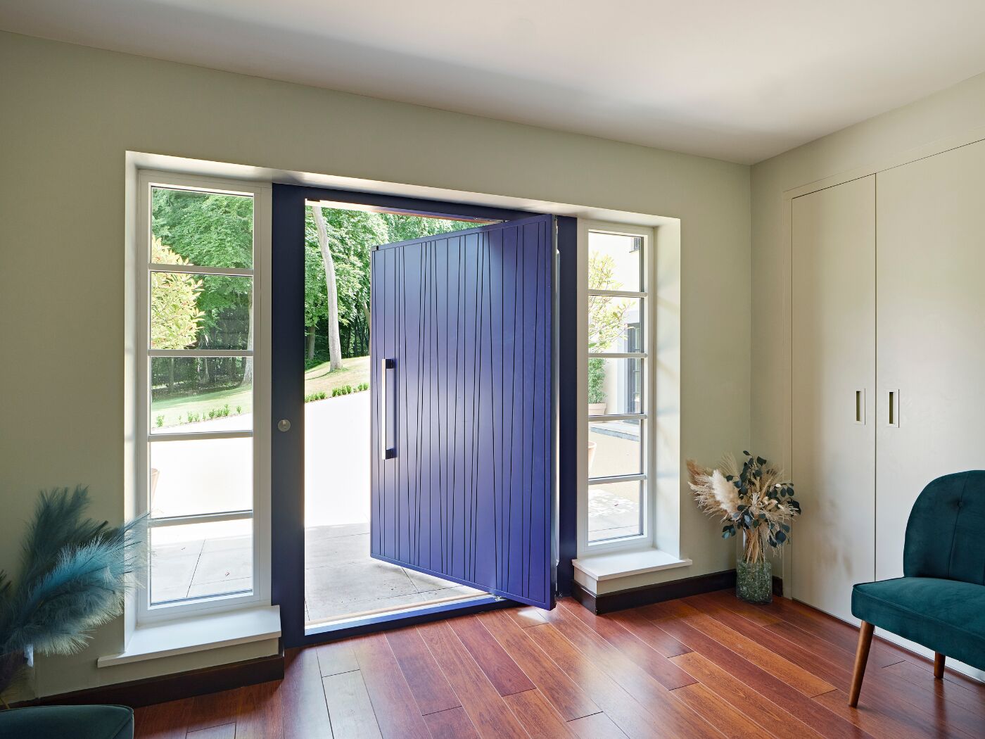 A pivot door in stunning cobalt blue opening onto a generous hall with storage and seating.