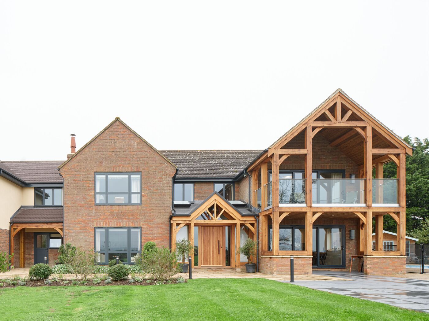 The oak porch echoes the covered balcony with pitched roof and frames the iroko front door.