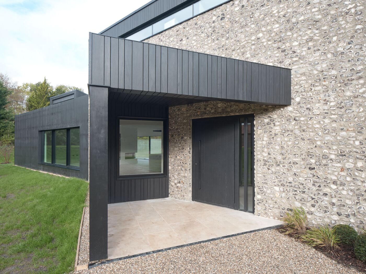 The oak door in ebony oil contrasts the double height flint façade and portico.