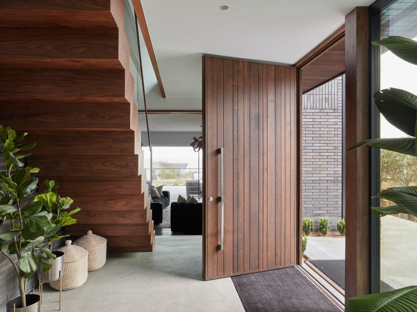 A welcoming hallway featuring custom staircase, plants and Rondo V door finished in walnut oil.